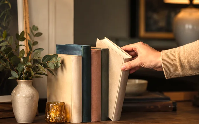 A hand selecting one book from a small stack on a table
